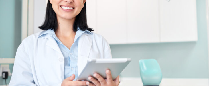 Young female caucasian dentist wearing a labcoat and smiling while using a digital tablet in her office. Dental hygiene is important to your wellbeing