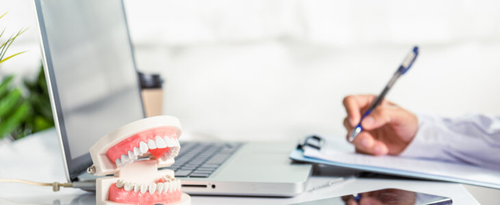 Oral dental. Dentist doctor in uniform writing information of patient in paperwork checklist on clipboard on desk office, teeth model, X-ray on laptop screen, prescription medical dental healthcare