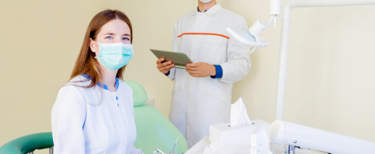Young dentists students in clinic in workplace with tool and equipment. Man male and female woman in white medical gown, mask and glasses with tablet.