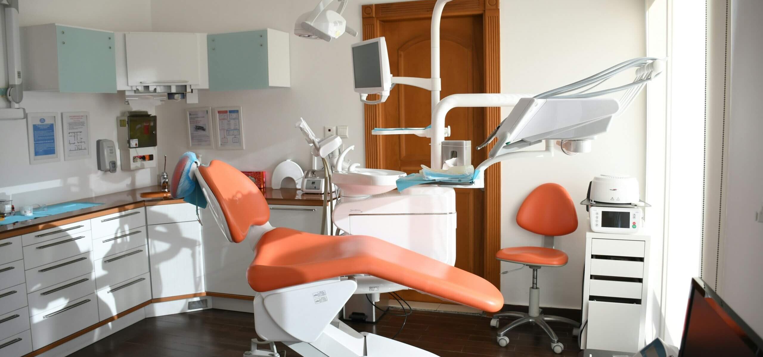 Inside of a dental office with an orange dentists chair